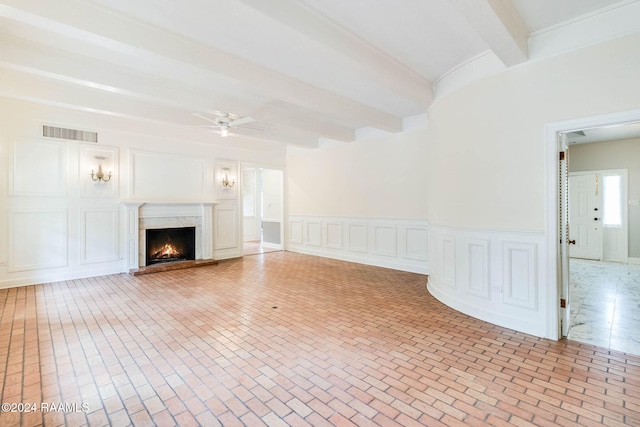 unfurnished living room with a high end fireplace, ceiling fan, and beam ceiling