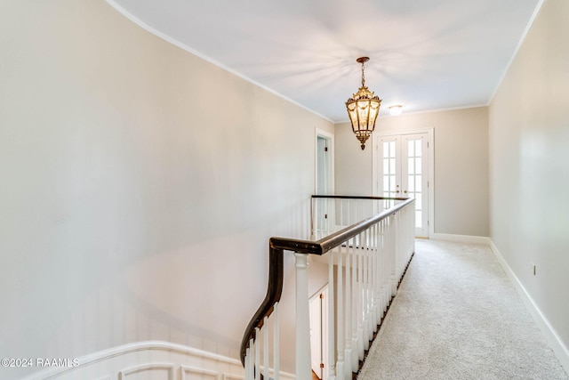 corridor with light carpet, crown molding, and an inviting chandelier