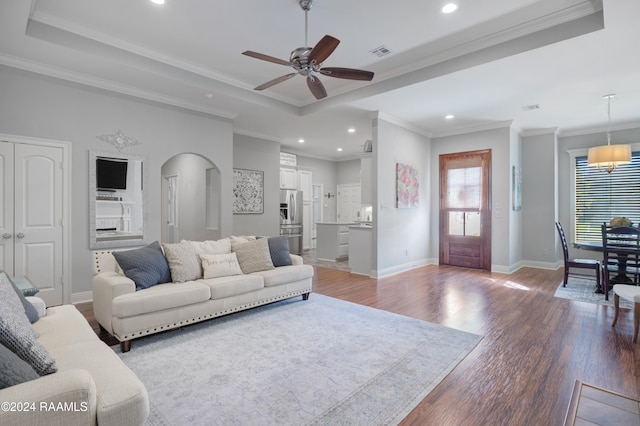 living room with dark hardwood / wood-style floors, a raised ceiling, ceiling fan, and crown molding