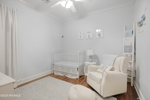 bedroom featuring ceiling fan, dark hardwood / wood-style flooring, a crib, and crown molding