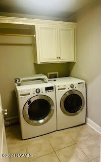 clothes washing area with cabinets, washing machine and clothes dryer, and light tile patterned floors