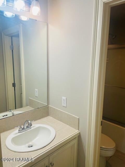 full bathroom featuring vanity, shower / bath combination with glass door, and toilet