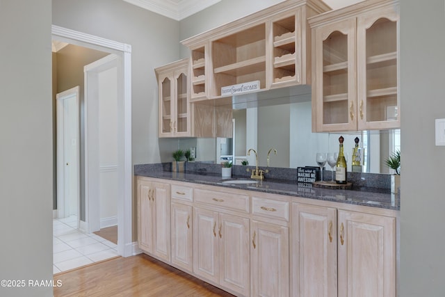 kitchen with light wood-type flooring, light brown cabinets, dark stone counters, and sink