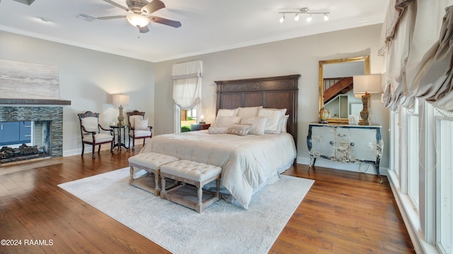 bedroom with dark wood-type flooring, a stone fireplace, crown molding, and ceiling fan