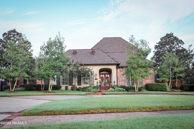 french country inspired facade with a front yard, french doors, brick siding, and a shingled roof