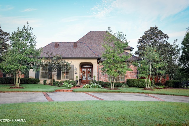 french provincial home with a front lawn, brick siding, and a shingled roof