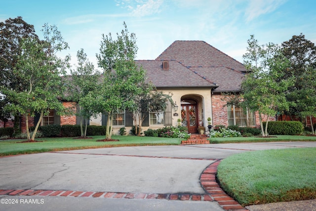 view of front of property featuring a front yard, roof with shingles, and brick siding