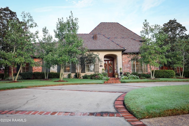 view of front facade featuring a front lawn, roof with shingles, and brick siding