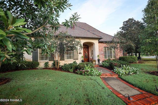 view of front facade with a front lawn, a shingled roof, and brick siding