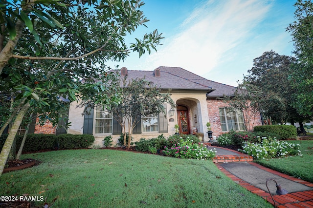 view of front of house with a front yard, brick siding, and roof with shingles