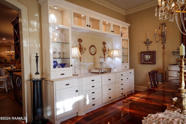 bar with dark hardwood / wood-style floors, ornamental molding, a notable chandelier, white cabinets, and light stone counters