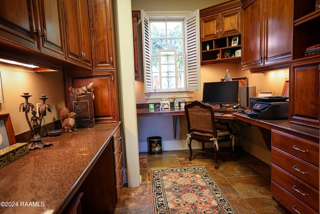 office area featuring built in desk, dark stone finish flooring, and baseboards