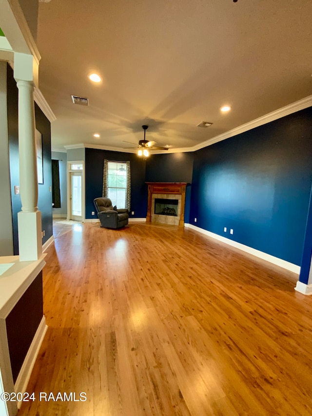 unfurnished living room featuring a tile fireplace, ornate columns, ceiling fan, crown molding, and light hardwood / wood-style flooring