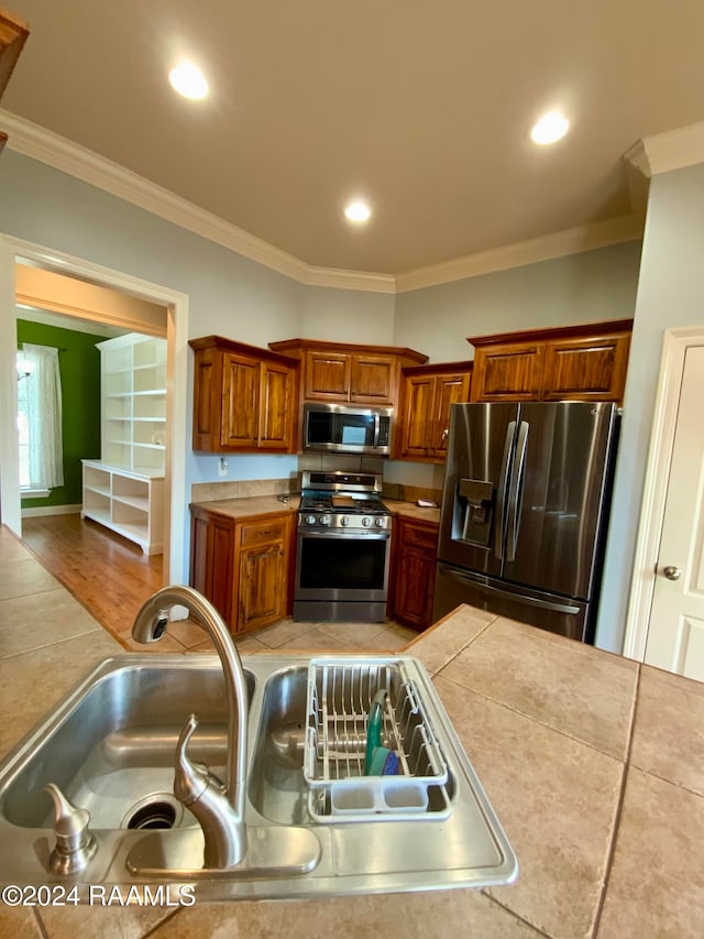 kitchen with ornamental molding, hardwood / wood-style floors, appliances with stainless steel finishes, and tile counters