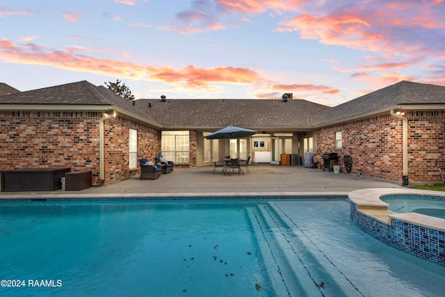 pool at dusk with an in ground hot tub, a patio area, and grilling area