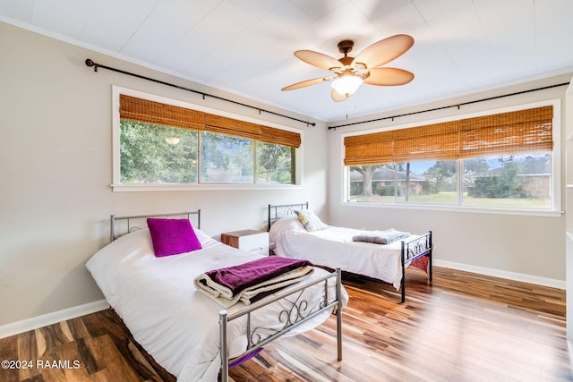 bedroom with multiple windows, wood-type flooring, crown molding, and ceiling fan