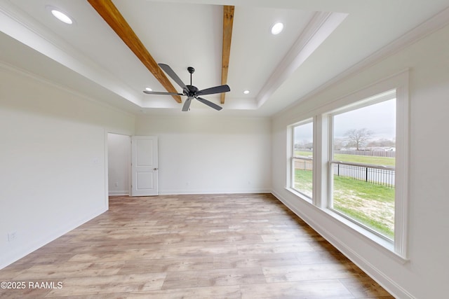 empty room featuring light wood-style floors, a tray ceiling, and ornamental molding