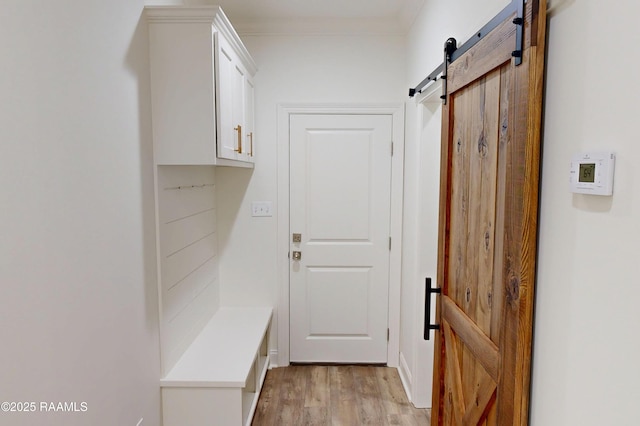 mudroom featuring light wood-type flooring, a barn door, and ornamental molding