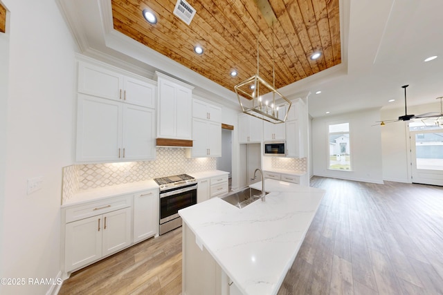 kitchen with a center island with sink, white cabinets, stainless steel range with gas stovetop, a tray ceiling, and a sink