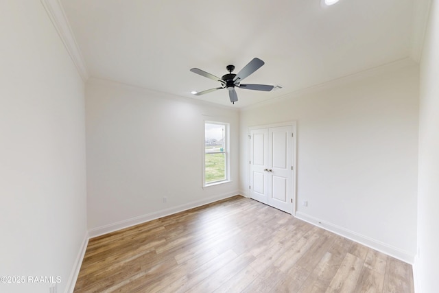 spare room featuring a ceiling fan, baseboards, crown molding, and light wood finished floors