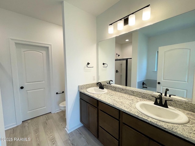 bathroom featuring toilet, wood finished floors, a stall shower, and a sink