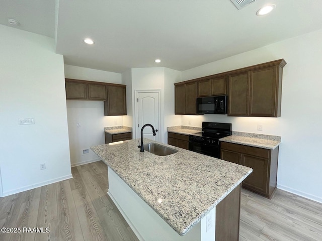 kitchen with black appliances, light stone counters, an island with sink, and a sink