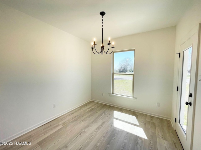 spare room with a chandelier, light wood-style flooring, and baseboards