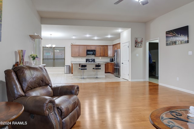 living room with light wood-type flooring and ceiling fan with notable chandelier