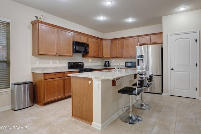 kitchen with a breakfast bar, light stone countertops, a kitchen island with sink, black appliances, and sink