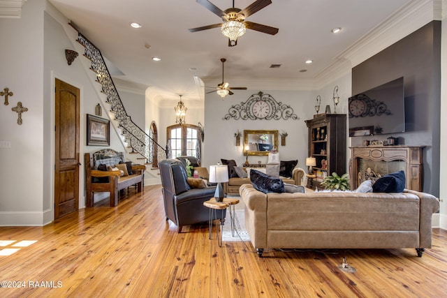 living room with ceiling fan with notable chandelier, ornamental molding, and light hardwood / wood-style flooring