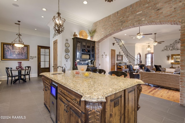 kitchen with wood-type flooring, light stone counters, crown molding, pendant lighting, and an island with sink