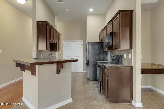 kitchen featuring dark brown cabinetry, black appliances, sink, a kitchen bar, and decorative backsplash