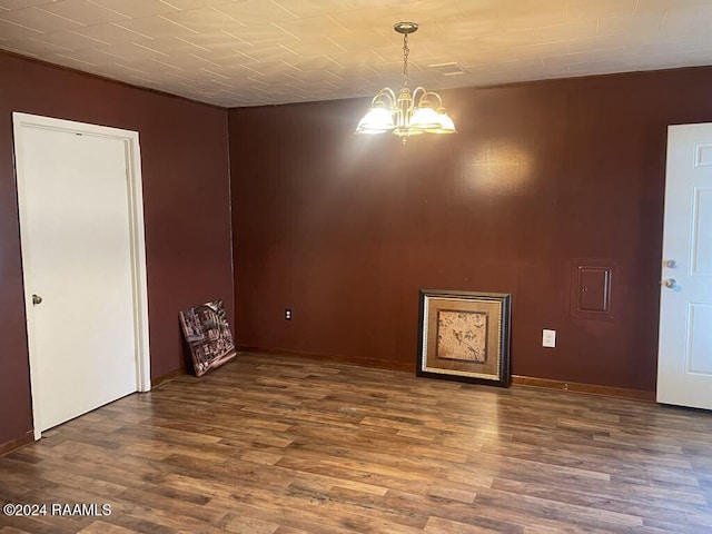 spare room with dark hardwood / wood-style floors and an inviting chandelier