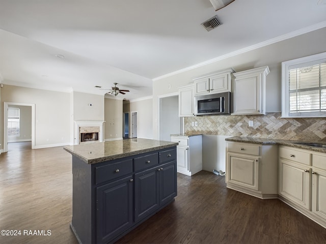 kitchen featuring decorative backsplash, dark hardwood / wood-style flooring, dark stone counters, ceiling fan, and a kitchen island