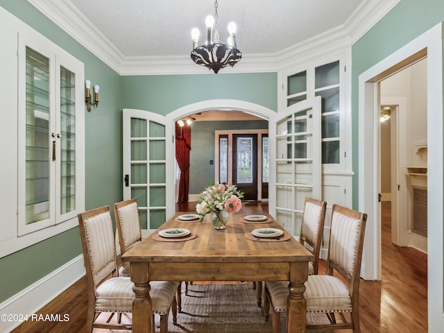 dining room with a textured ceiling, hardwood / wood-style floors, a chandelier, crown molding, and french doors