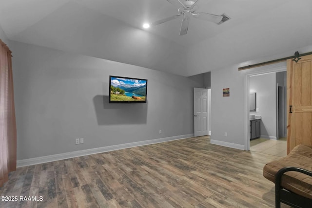 unfurnished room featuring ceiling fan, a barn door, lofted ceiling, and light wood-type flooring