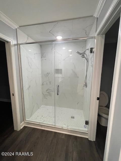 bathroom featuring toilet, wood-type flooring, an enclosed shower, and ornamental molding