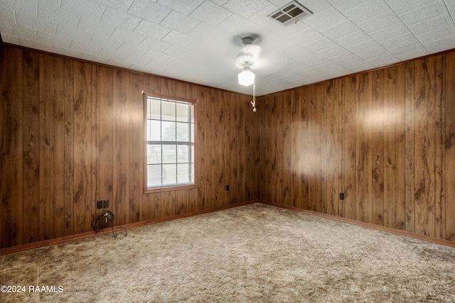 carpeted spare room featuring wood walls and ceiling fan