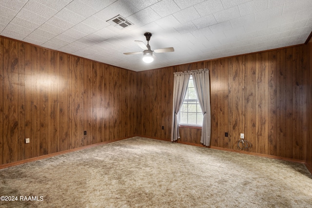 carpeted spare room featuring wood walls and ceiling fan