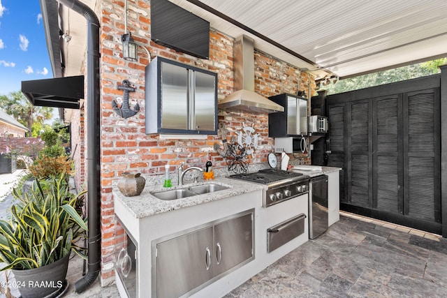 kitchen with stainless steel appliances, brick wall, sink, light stone countertops, and wall chimney range hood