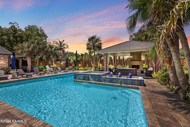 pool at dusk with an outdoor fireplace, a patio, and an in ground hot tub