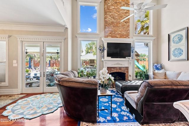 living room featuring a brick fireplace, a towering ceiling, wood-type flooring, and a healthy amount of sunlight