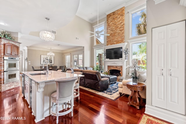 kitchen featuring a center island with sink, a towering ceiling, hanging light fixtures, stainless steel double oven, and a kitchen breakfast bar