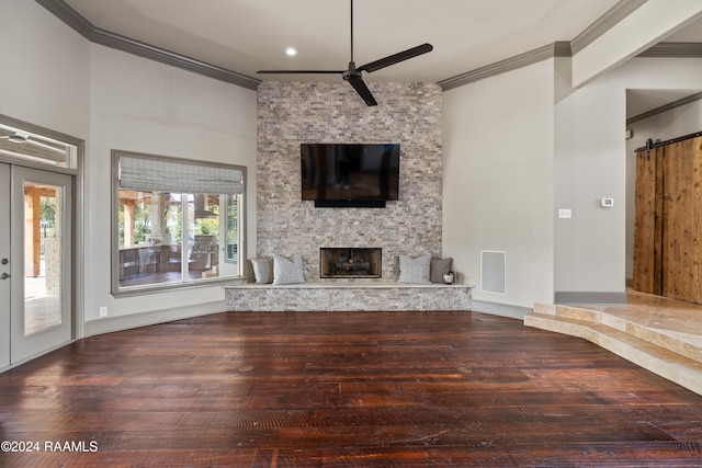 unfurnished living room featuring hardwood / wood-style flooring, a fireplace, ornamental molding, and a barn door