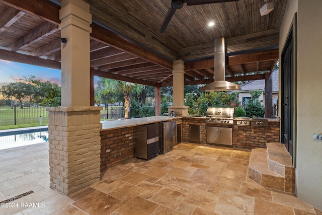 patio terrace at dusk featuring grilling area, an outdoor kitchen, and ceiling fan