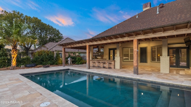 pool at dusk featuring a patio and exterior bar