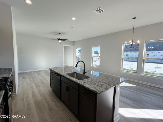 kitchen with black appliances, an island with sink, sink, light wood-type flooring, and light stone counters