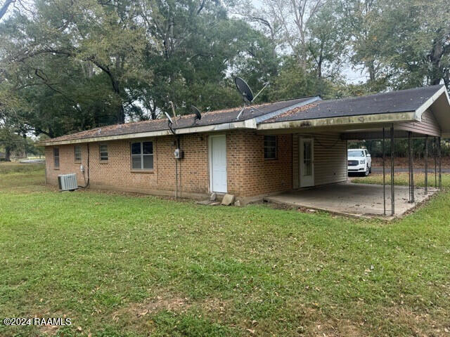 rear view of property featuring central air condition unit, a yard, and a carport