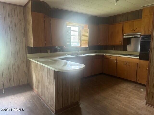 kitchen with black appliances, dark hardwood / wood-style flooring, wood walls, sink, and kitchen peninsula