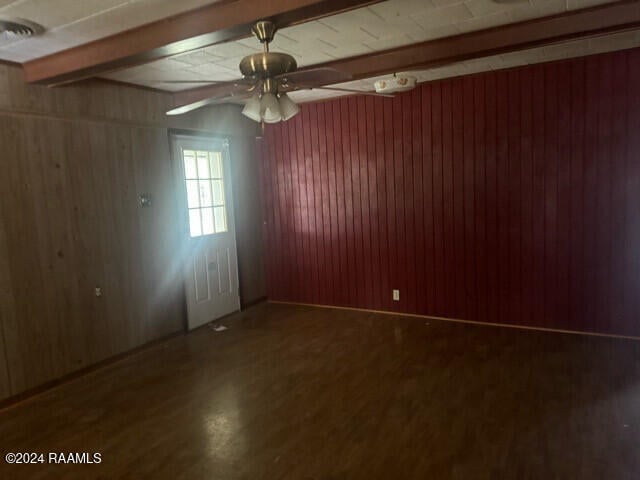 spare room featuring beam ceiling, wooden walls, and dark hardwood / wood-style flooring